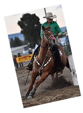 A barrel racer and her horse round a barrel.