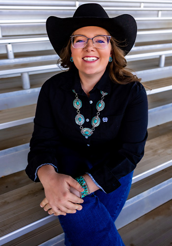 Wearing a black cowboy hat and blouse along with a big smile, Maddie Renfroe sits on the bleachers.