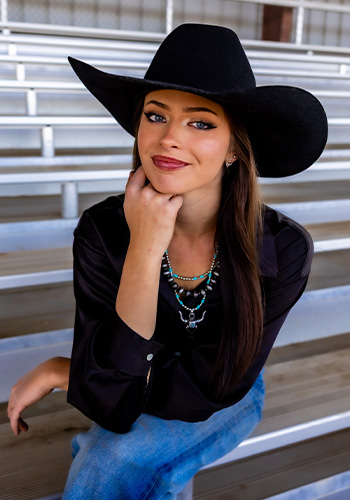 Margo Schaffer at the fairgrounds sits with her chin on her hand and wears a black cowboy hat and top.